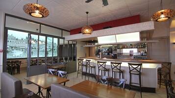 A restaurant with a bar area, high chairs, and a view of a cityscape through large windows.