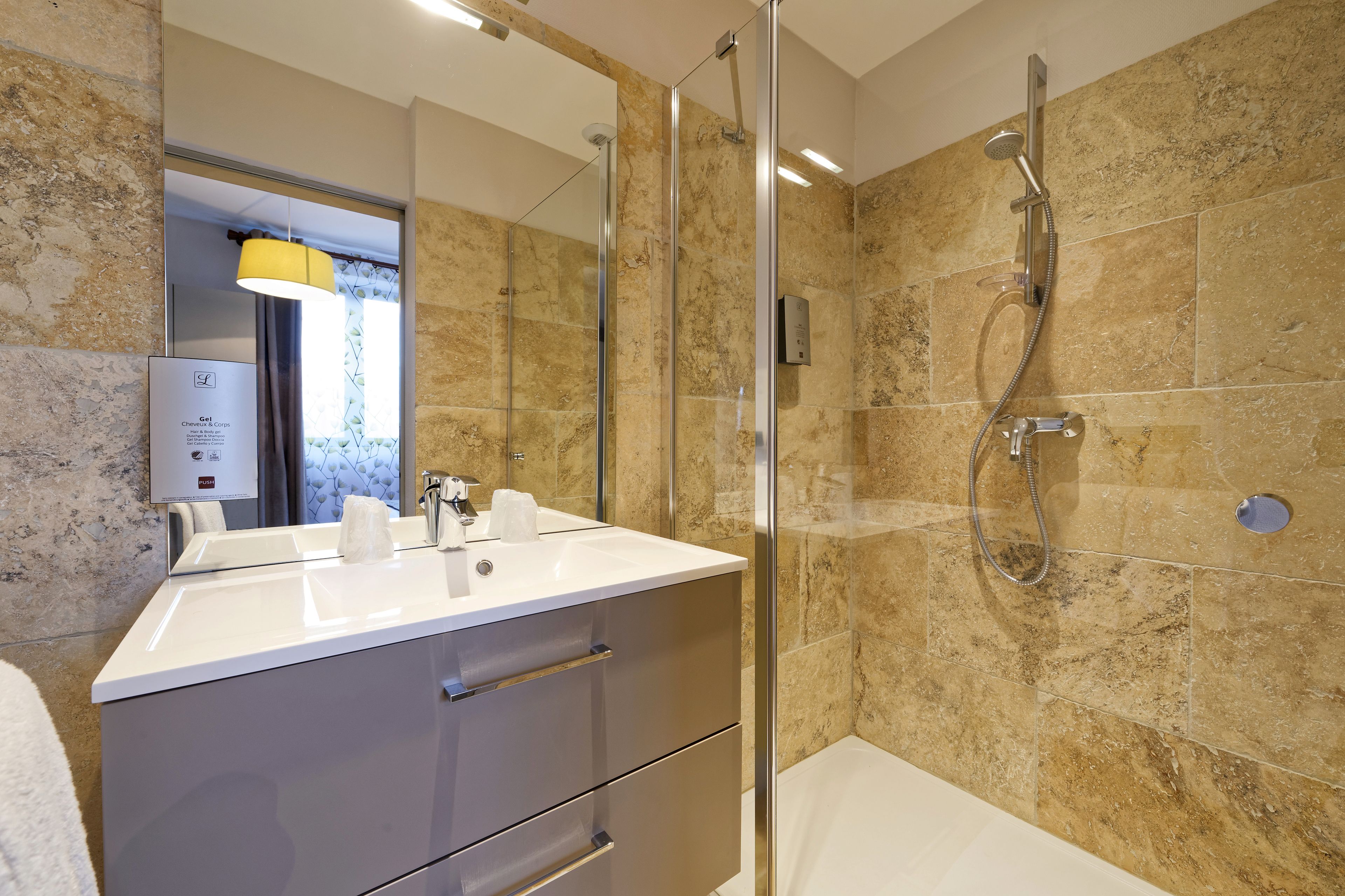 Une salle de bain moderne avec une douche à l’italienne en verre, un lavabo blanc et un mur de douche recouvert de carreaux de marbre.