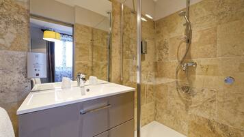 Une salle de bain moderne avec une douche à l’italienne en verre, un lavabo blanc et un mur de douche recouvert de carreaux de marbre.