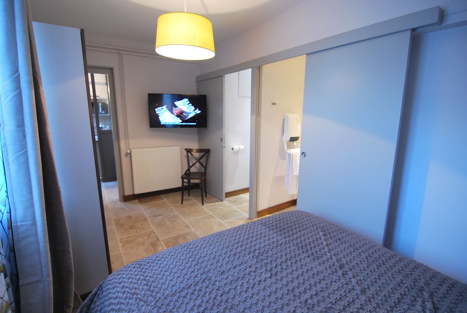 A bedroom with a bed, a television on the wall, a chair, and a bathroom door.