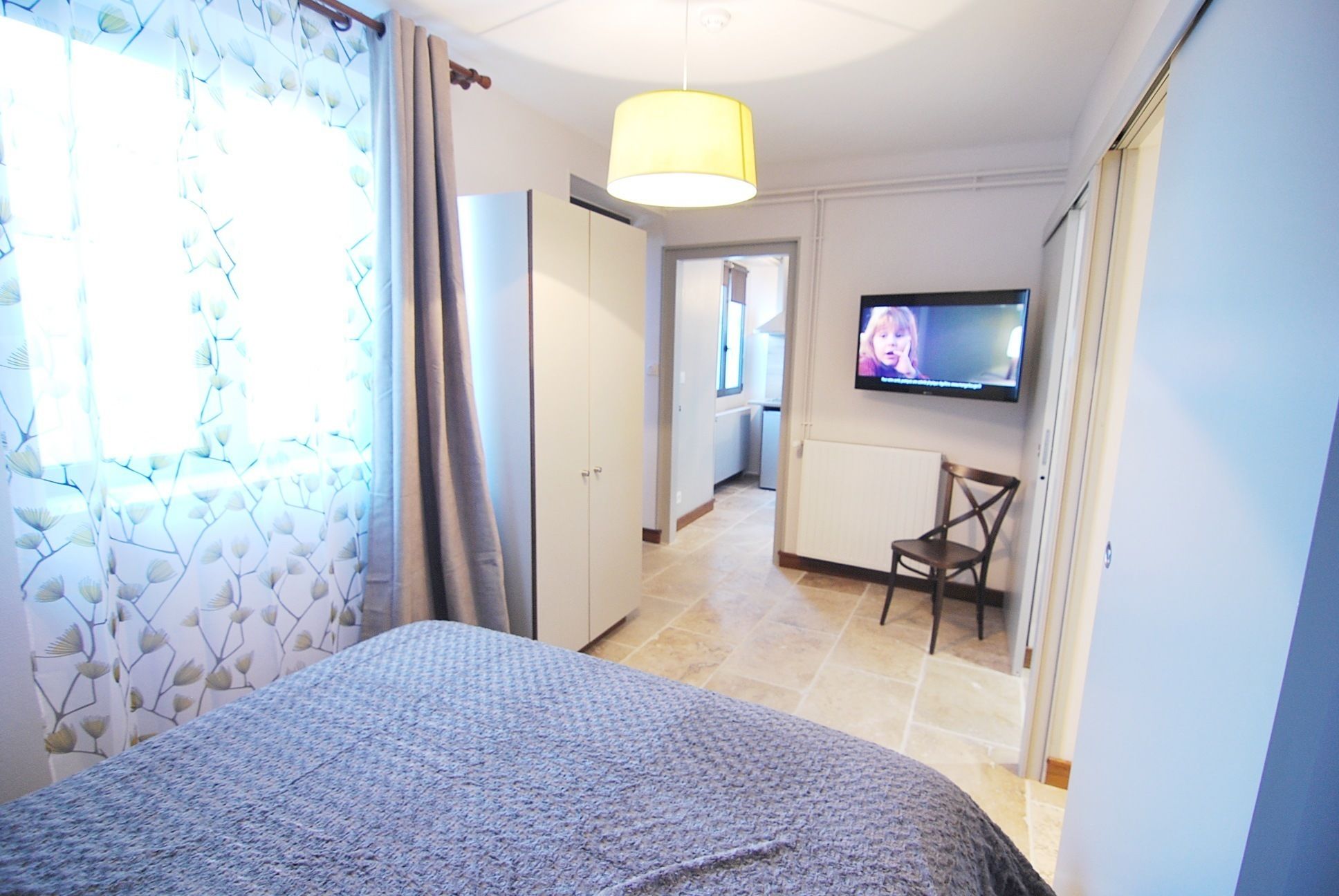 A hotel room with a bed, a TV, a chair, and a view of the hallway.
