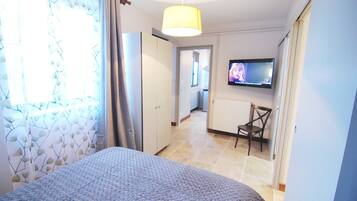 A hotel room with a bed, a TV, a chair, and a view of the hallway.