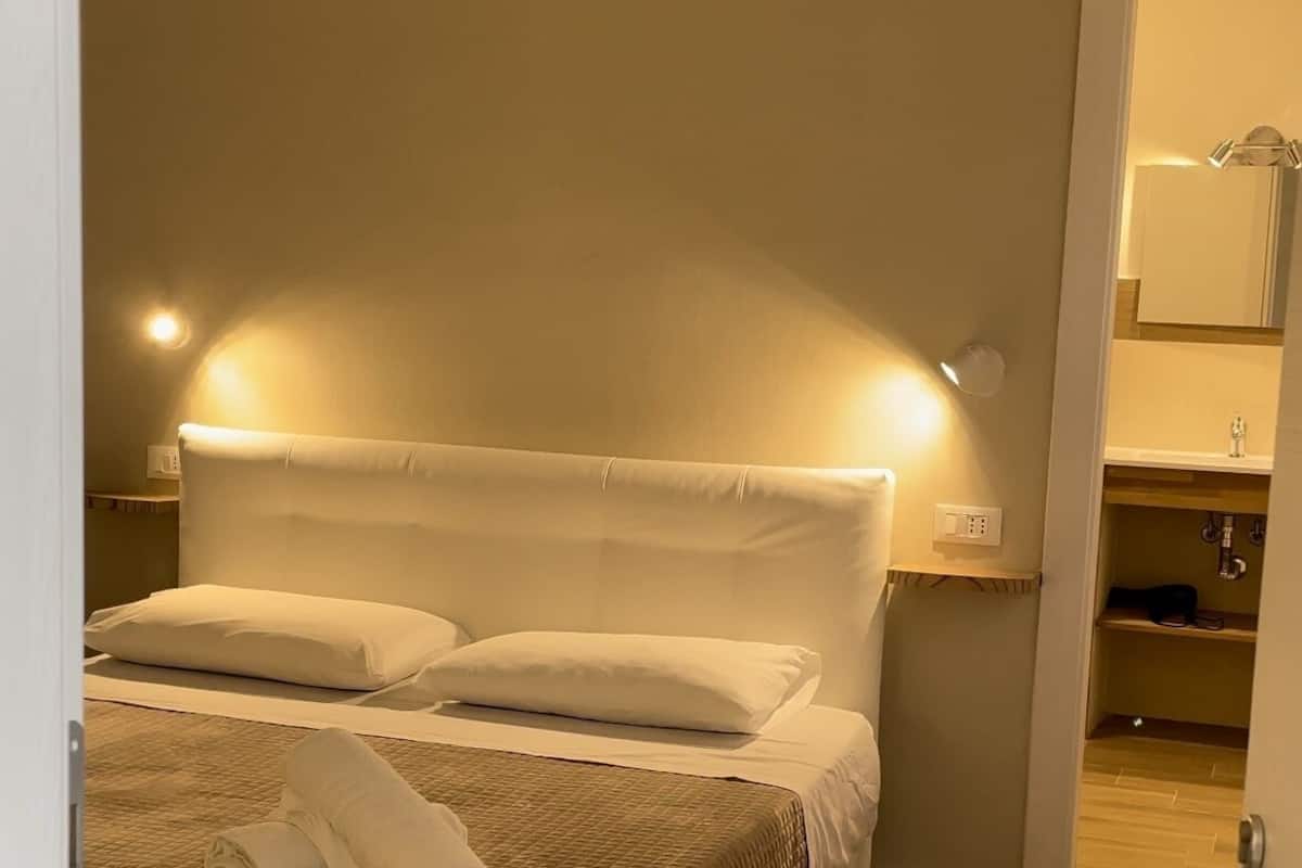 A neatly made bed with a quilted blanket and two pillows, a bedside lamp, and a wall-mounted air conditioner.