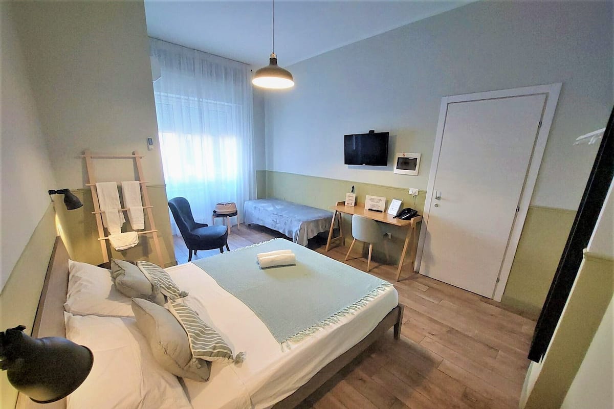 A hotel room with a bed, a desk, a chair, a TV, and a wardrobe.