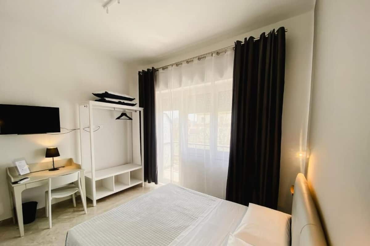 A hotel room with a bed, a desk, a TV, and a window with curtains.