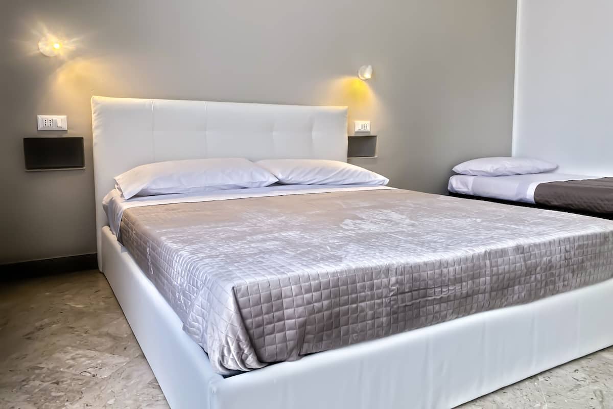 A modern hotel room with a large bed, two bedside tables, and wall-mounted lighting.