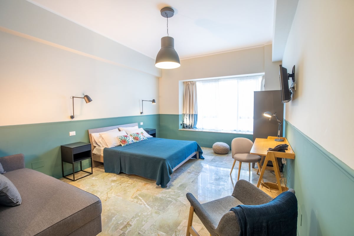A hotel room with a bed, a desk, a chair, a TV, and a window.