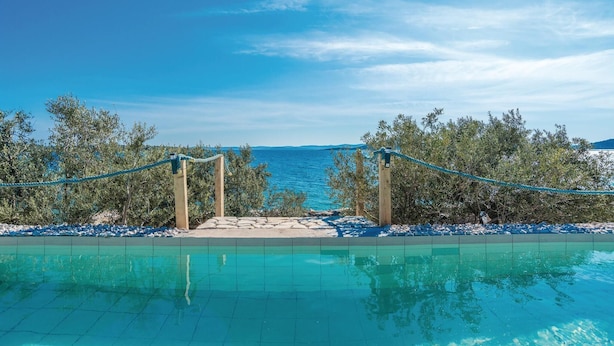 Ein klares, blaues Schwimmbecken mit Blick auf das Meer, umgeben von Bäumen und einer Seilsperre.