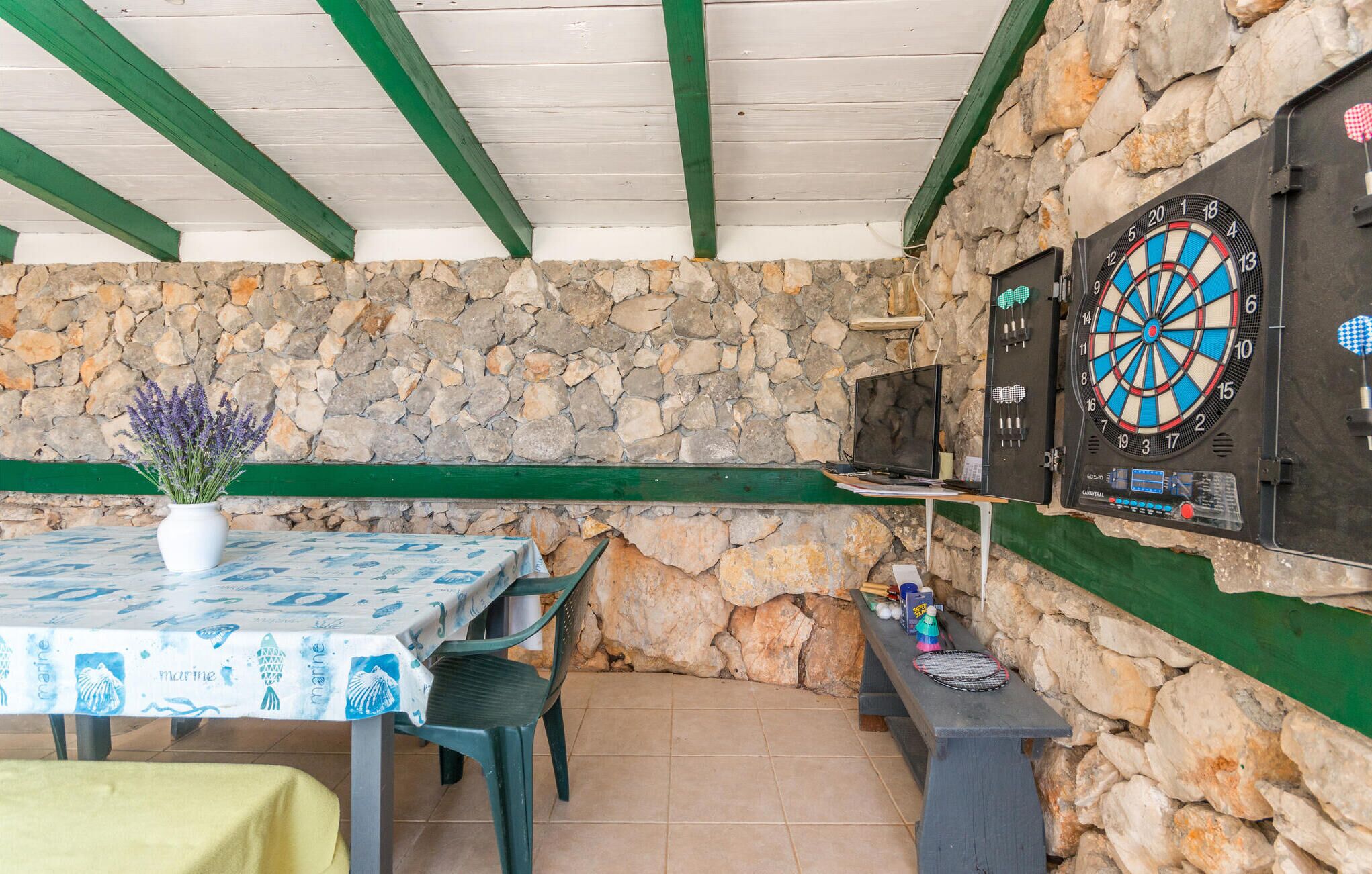 An outdoor dining area with a stone wall, a dartboard, and a table with a marine-themed tablecloth.