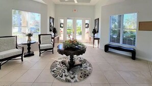 A spacious lobby with a high ceiling, a central round table with a floral arrangement, and a bench along the wall. - Luxury Waterfront Condo Close to Fort Myers Beach and Golf Courses! (Fort Myers)