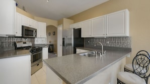 A kitchen with white cabinets, a stainless steel refrigerator, a microwave, and a stove. - Spacious Southwestern Sunny Casita (Tucson)