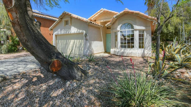 A house with a garage, a large tree in front, and a garden with various plants. - Spacious Southwestern Sunny Casita (Tucson)