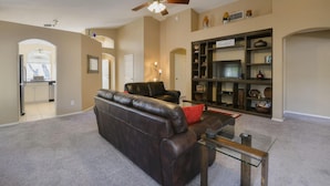 A spacious living room with a dark leather sofa, a glass coffee table, and a ceiling fan. - Spacious Southwestern Sunny Casita (Tucson)