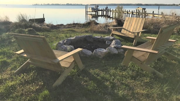 Un entorno junto al lago con una fogata y sillas de madera.