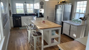 Una cocina con armarios blancos, una mesa de madera y un refrigerador.