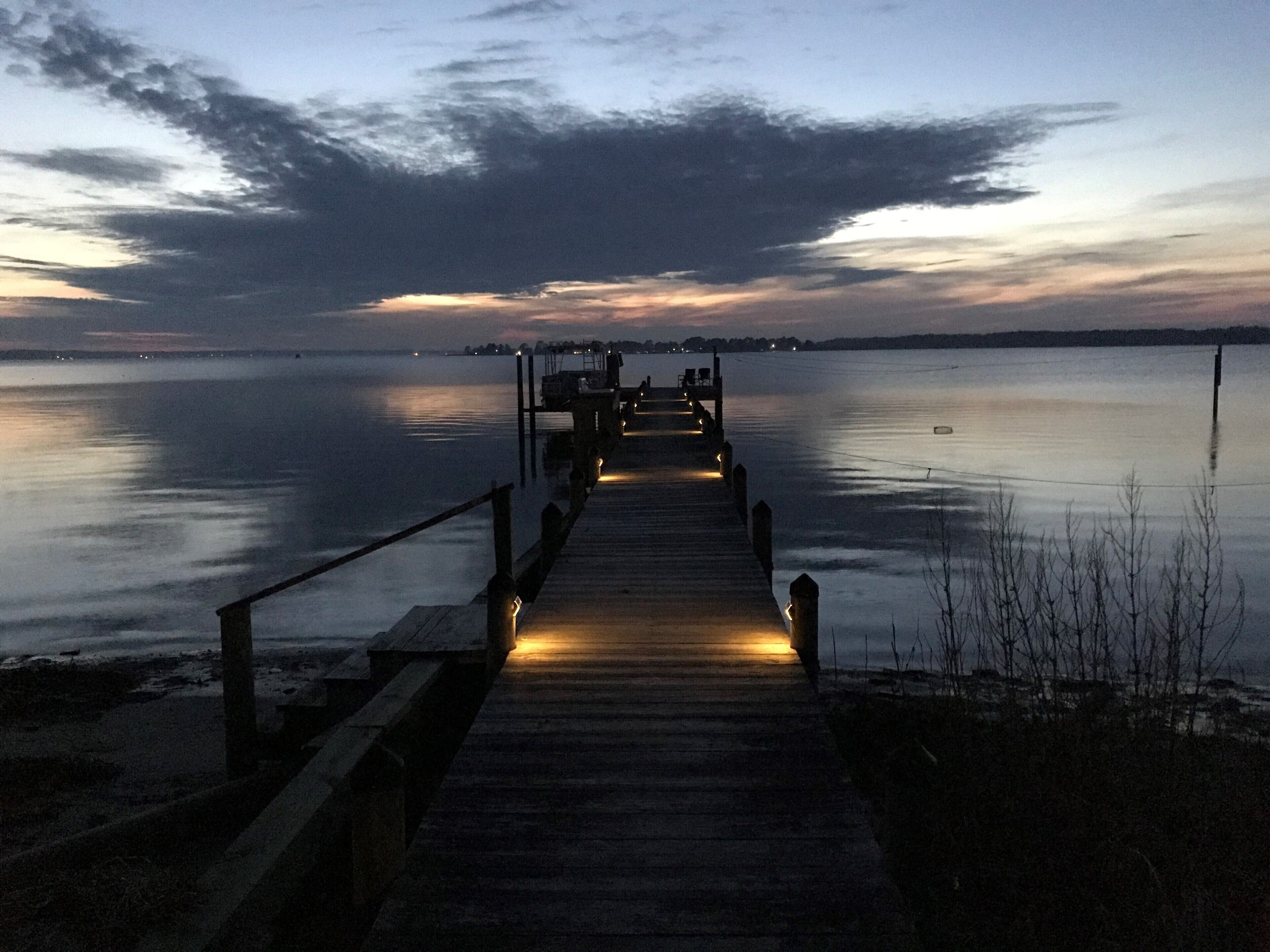 A wooden pier extending into calm water with a cloudy sky above.
