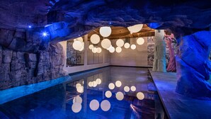 En indendørs swimmingpool med et moderne design, kendetegnet ved en stenvæg og hængende kugleformede lamper.
