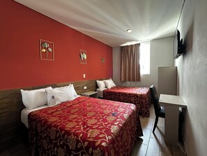 A hotel room with two beds, a desk, and a TV on the wall. - Hotel Teresita (Puebla)