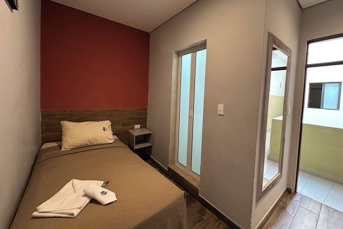 A bedroom with a bed, a nightstand, a window, and a door leading to a balcony.