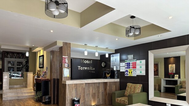 Uma área de recepção de hotel com um balcão de madeira, um relógio e um espaço de estar com um sofá verde e uma mesa de centro.