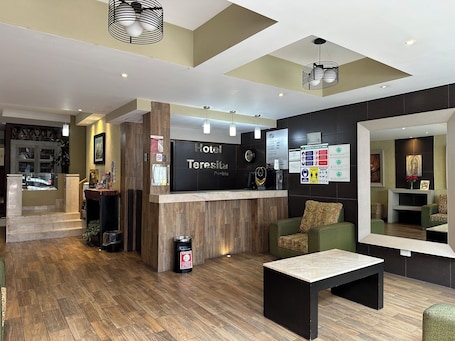 A hotel reception area with a wooden reception desk, a clock, and a seating area with a green sofa and a coffee table.