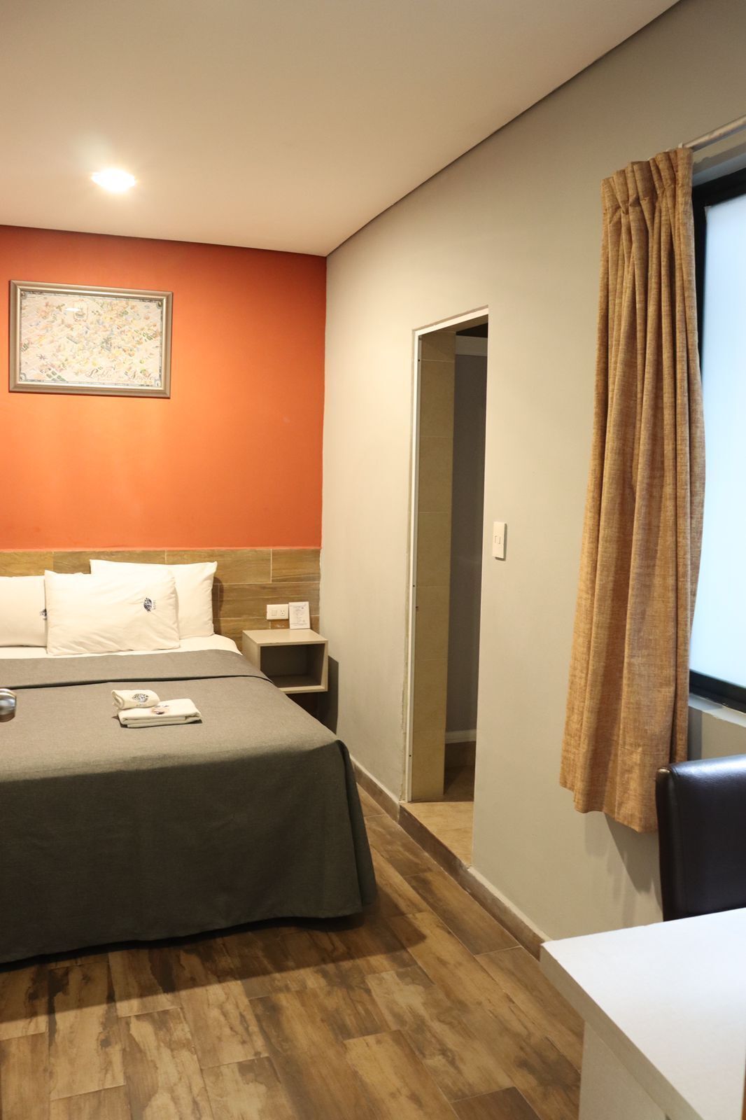 Habitació d'hotel amb llit, una tauleta de nit, escriptori, finestra amb cortines i un quadre al mur.