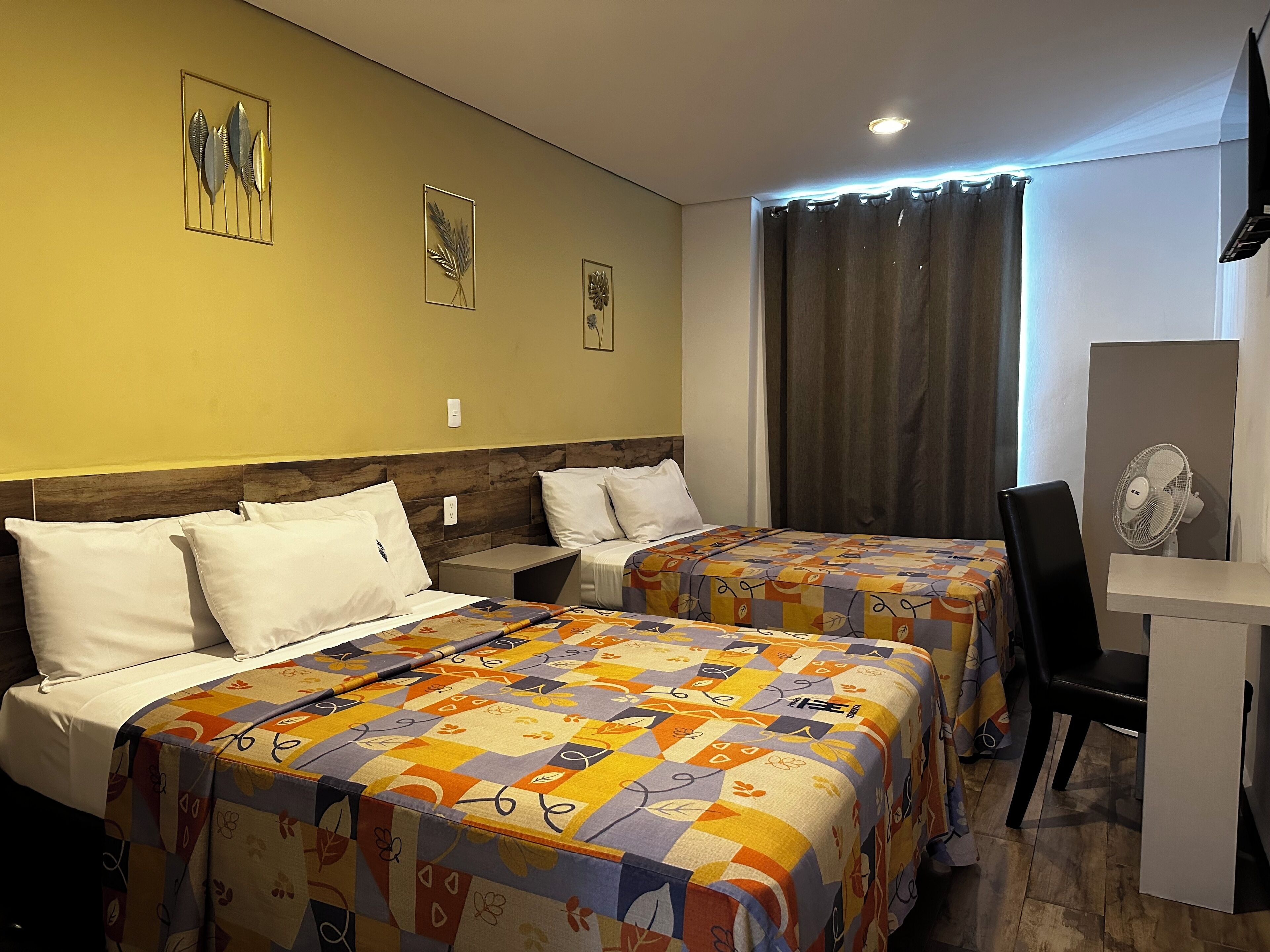 A hotel room with two beds, a desk, and a chair. There are decorative wall art pieces above the beds.