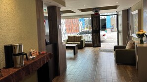 Um saguão de hotel com balcão de recepção, área de estar e vista para a rua.