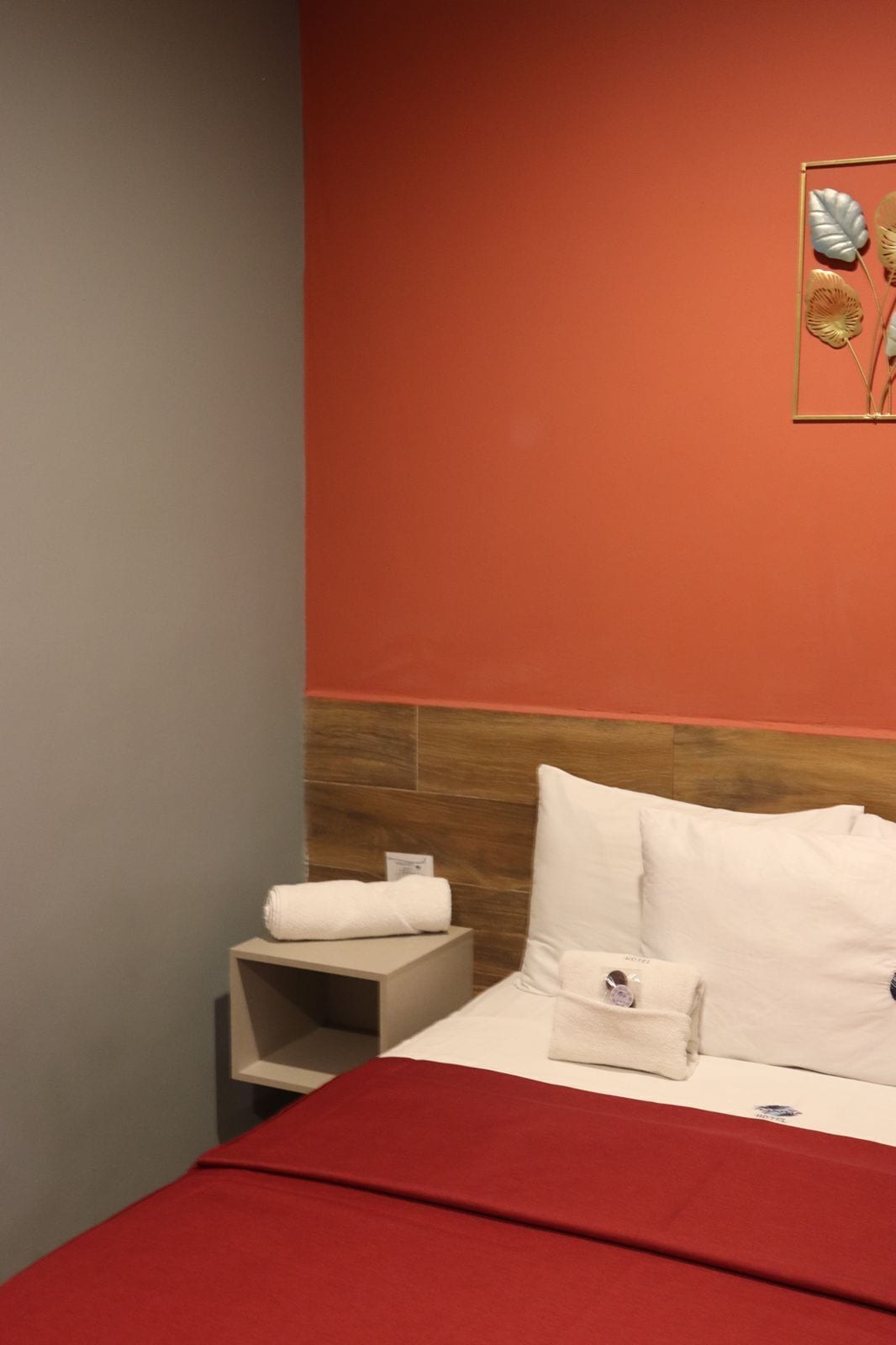 A hotel room with a red bedspread, white pillows, and a wooden headboard.