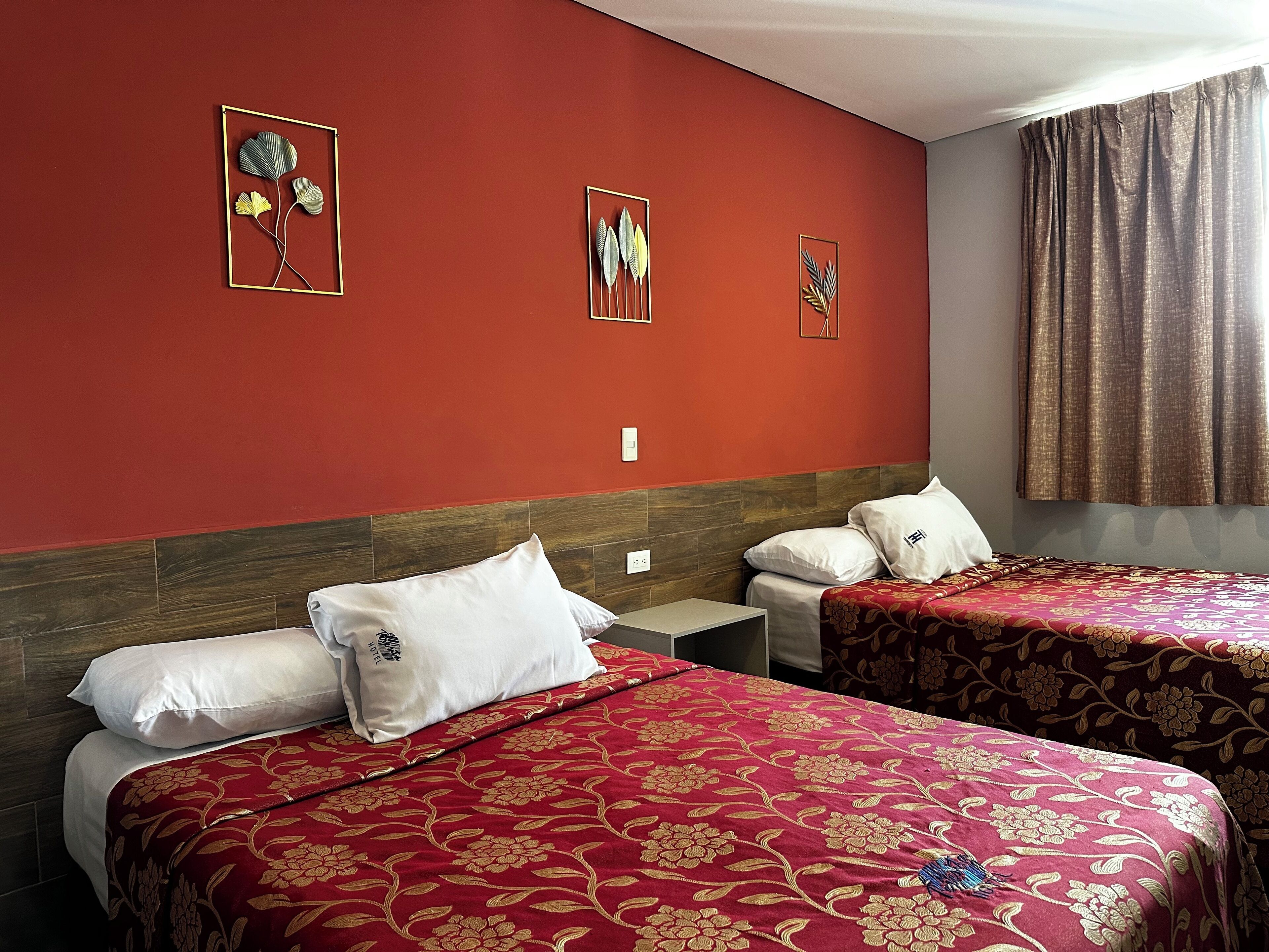 Une chambre d’hôtel avec deux lits, des couvre-lits à motifs floraux rouges, des oreillers blancs et des œuvres d’art murales représentant des feuilles et des fleurs.