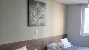 Quarto de hotel com duas camas, uma mesinha de cabeceira, uma obra de arte na parede e uma janela.
