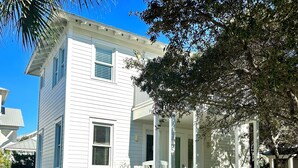 A two-story white house with a front porch, a covered entryway, and a small front yard with gravel and plants. - Happy Hour Cottage Steps Away from Beach (Panama City Beach)
