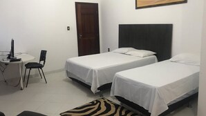 Une petite chambre propre, avec deux lits simples, un bureau avec une chaise et un tapis à motifs zébrés.