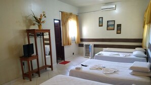 Une chambre d’hôtel avec deux lits, un téléviseur posé sur un meuble, une fenêtre avec des rideaux et un climatiseur fixé au mur.