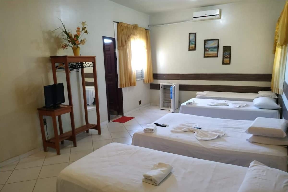 Quarto de hotel com duas camas, televisão sobre suporte, janela com cortinas e ar condicionado fixado na parede.