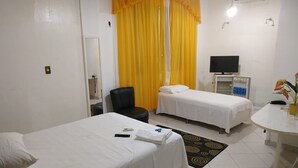 Une chambre d’hôtel avec deux lits simples, un bureau avec une chaise, une télévision et une salle de bain avec un miroir et des toilettes.
