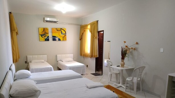Une chambre d’hôtel avec deux lits simples, une petite table avec des chaises, un vase de fleurs et un tableau au mur.