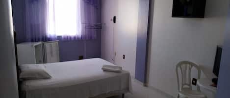 Un dormitorio con cama, una silla, una mesita, televisor montado en la pared y teléfono.
