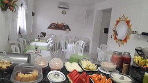 Une pièce avec des chaises en plastique blanc, une table sur laquelle sont disposés des aliments et un ventilateur au plafond.