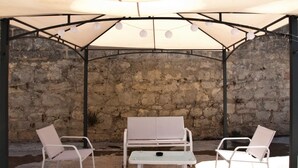 Un área de estar al aire libre con un muro de piedra de fondo, un porche cubierto y una mesa.