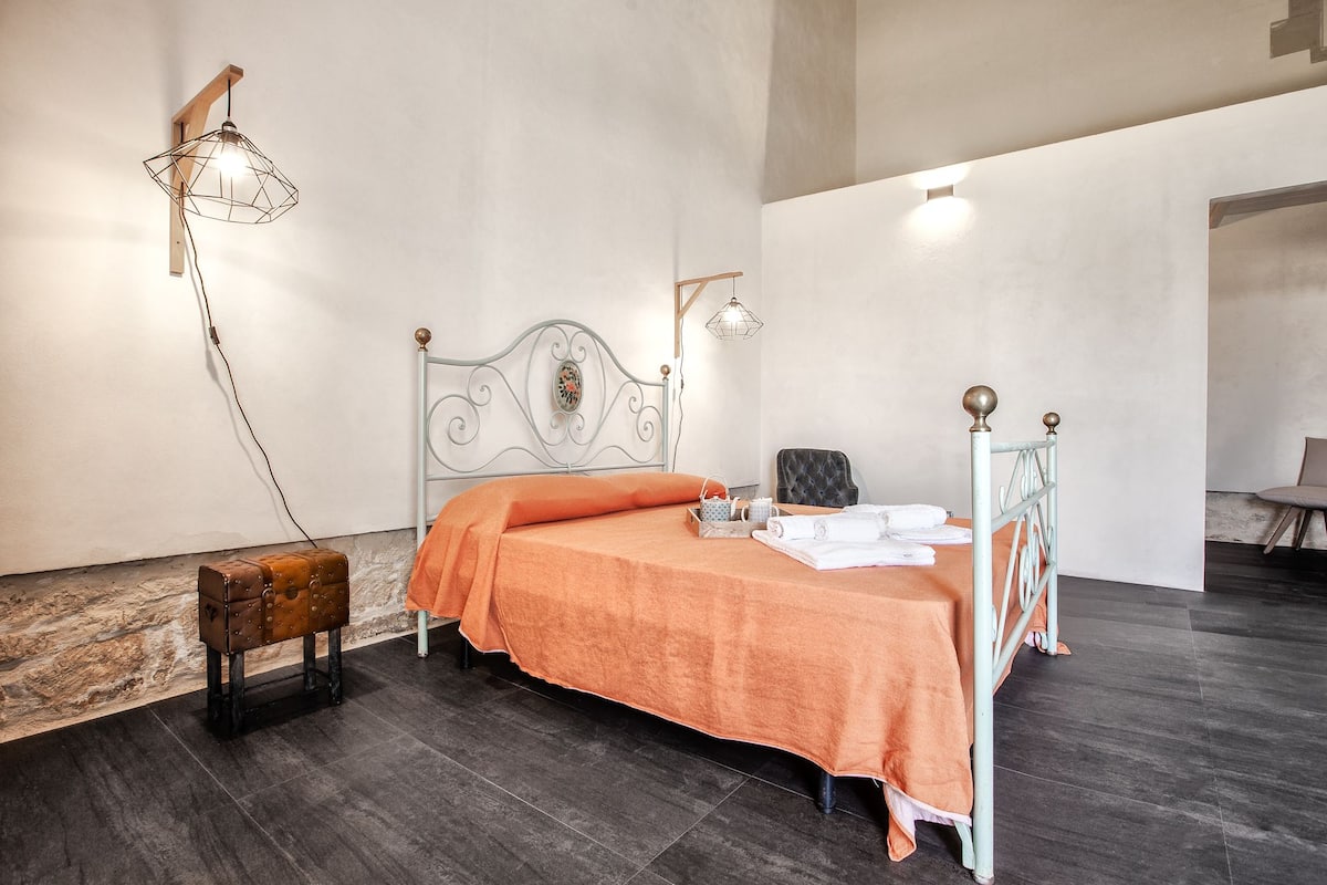 A bedroom with a bed, a chair, a suitcase, and a lamp.