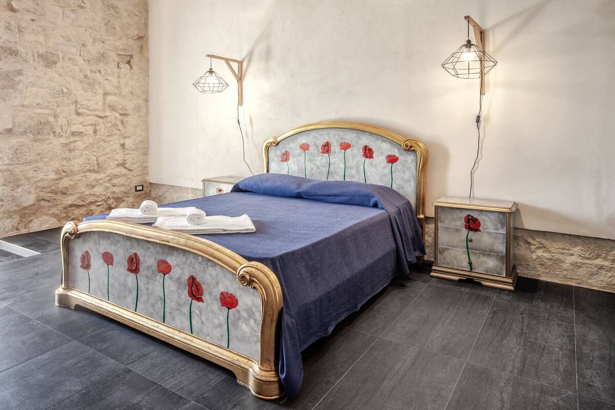 A bed with a floral headboard, a blue bedspread, and two bedside tables with lamps.