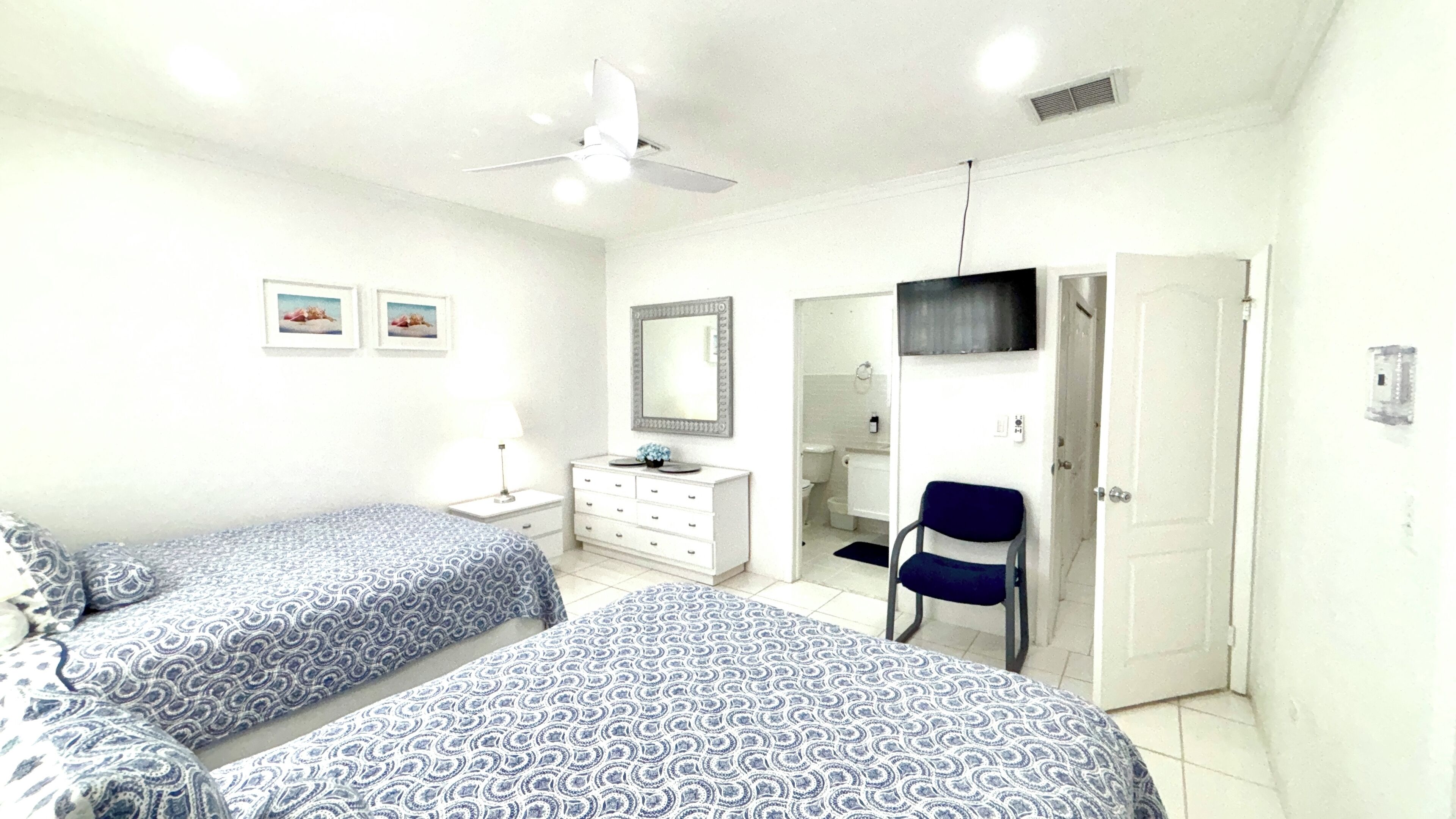 A bedroom with two beds, a dresser, a chair, a TV, and a door.