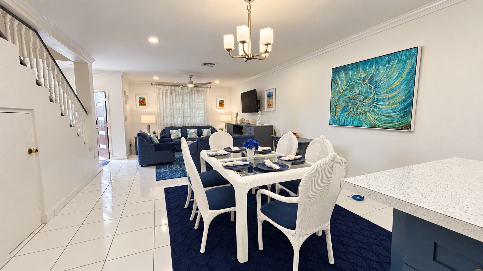 A modern dining area with a glass table, white chairs, and a blue rug.