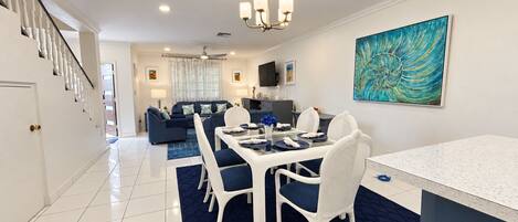 A modern dining area with a glass table, white chairs, and a blue rug.