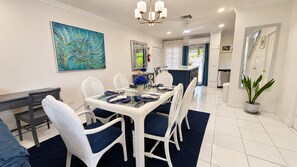 A dining area with a glass-top table, white chairs, and a blue rug.