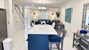 A modern kitchen with a central island, dining chairs, and a staircase leading to an upper level.