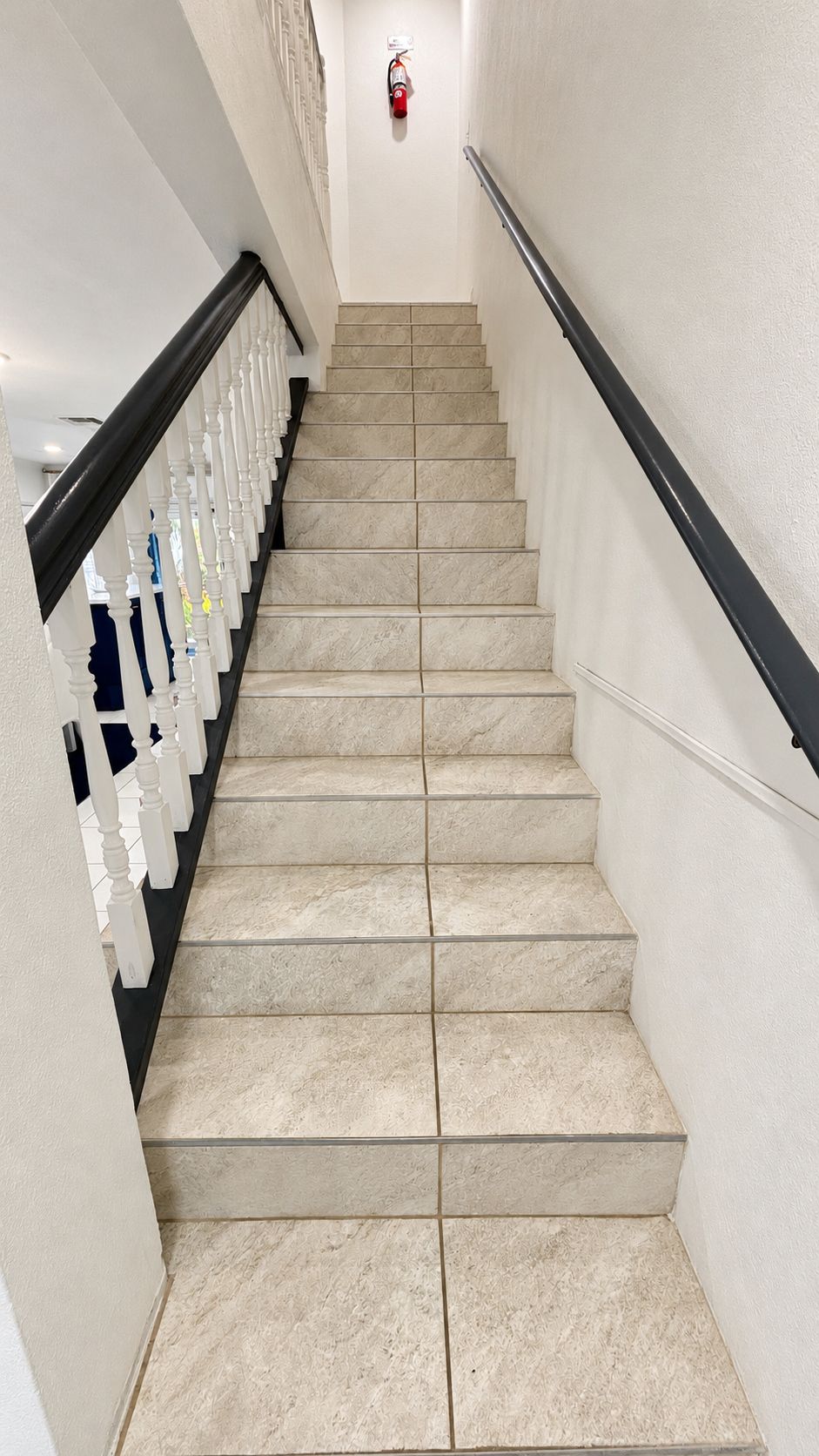 A staircase with beige tiles, white balusters, and a black handrail.
