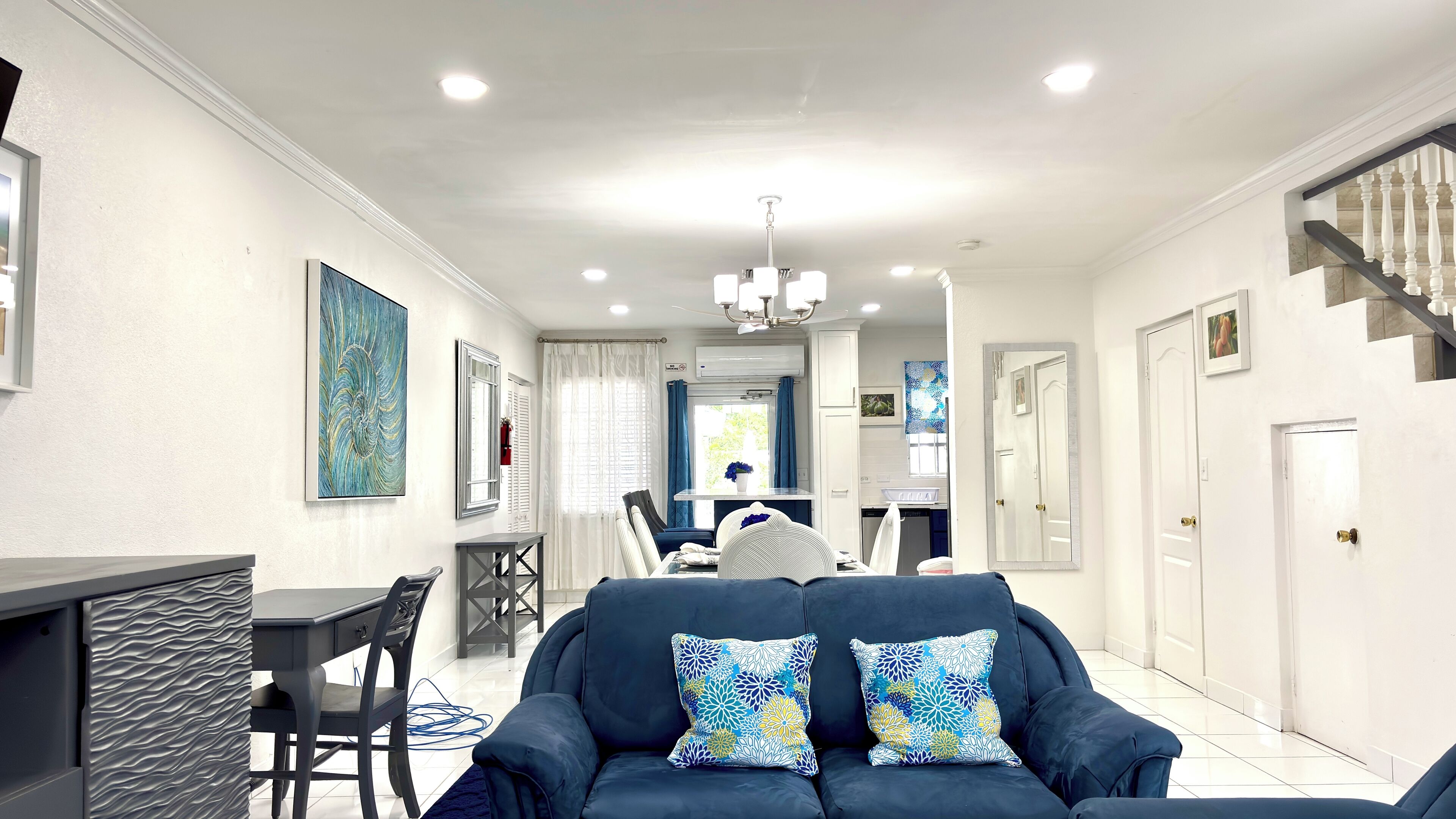 A modern living room with a dark blue sofa, a dining area with a table and chairs, and a staircase with white balusters.