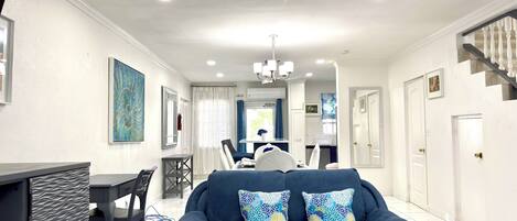 A modern living room with a dark blue sofa, a dining area with a table and chairs, and a staircase with white balusters.